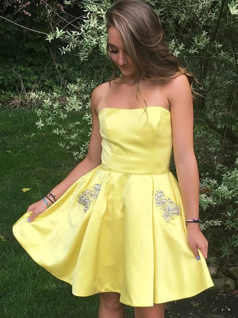 Elegant axelbandslös kort gul balklänning med fickor, A-linjeformad satin homecoming-klänning